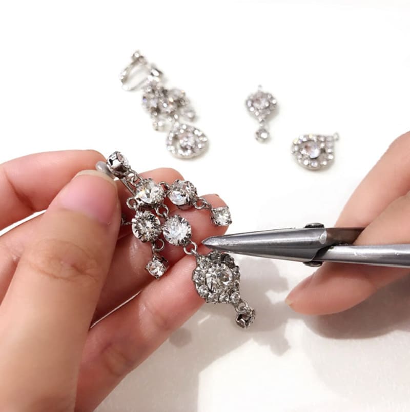 マリコ工房での手作業ろう付け加工の様子。職人がピンセットを使いクリスタルの爪どめ枠を一つひとつ丁寧に仕上げている。金属部分を最小限にすることで軽く美しいアクセサリーが完成する。